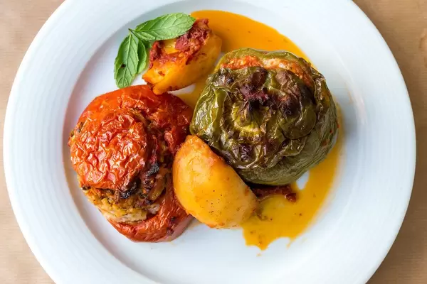 Griechisches Gericht "Gemista", mit roter und grüner gefüllter Tomate und Paprika, mit Reis, Pininenkernen, Minzblättern, Früchten und gelber Sauce