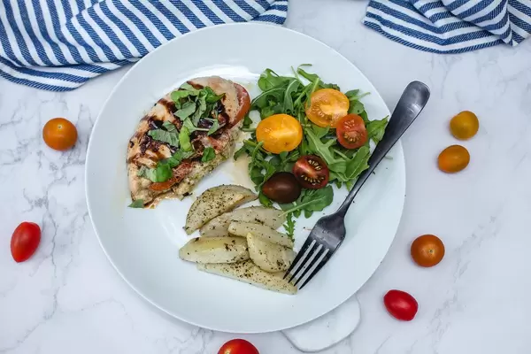 Griechisches Hühnerfleisch, mit Käse und getrockneten Tomaten gefüllt, neben Tomaten und einem grünen Salat