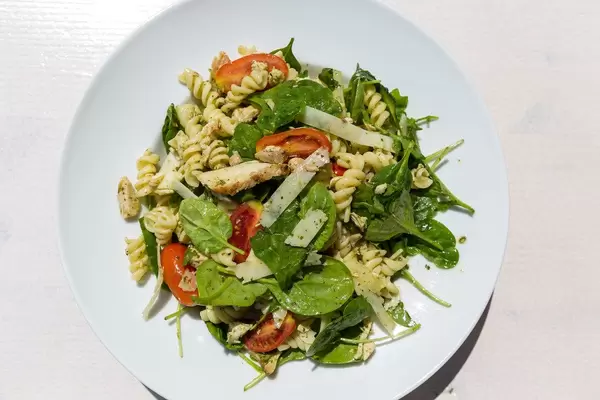 Griechisches Nudelgericht mit grünen Blättern, Tomaten und Parmesan