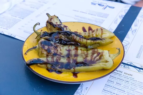 Grilled green Greek peppers with balsamic vinegar on yellow plate on menus