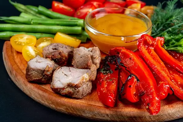 Grilled meat and vegetables on a wooden board with mango sauce