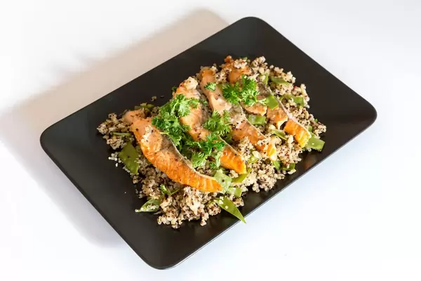 Grilled salmon slices on cauliflower quinova with parmesan chips on black plate