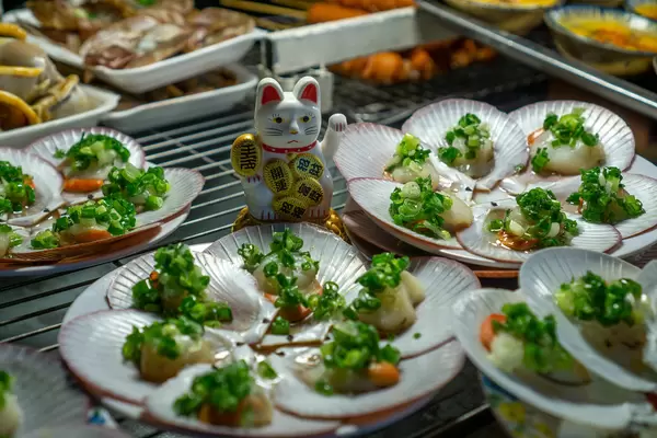 Grilled Scallops with Spring Onion on a Barbecue Grill with a Small Waving Cat as Decoration at a Nightmarket in Vietnam