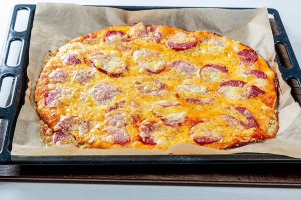 Große frische Pizza mit geräuchertem Wurst und Mozzarellakäse auf schwarzem Backblech