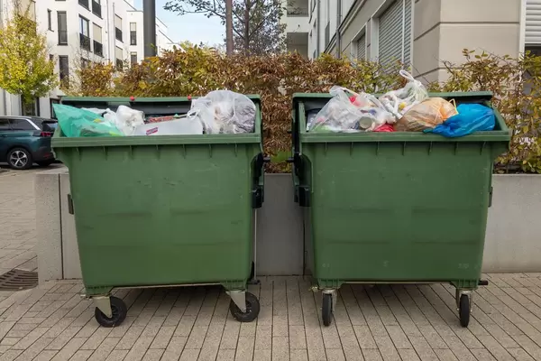 Große grüne Mülltonnen voll bis oben hin in einer Wohngegend