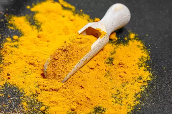 Ground turmeric in wooden scoop on black background