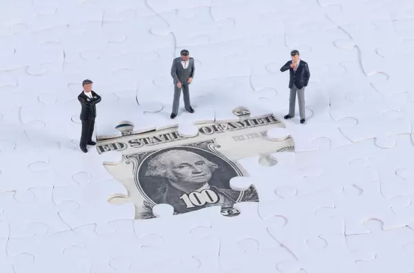 Group of miniature businessman with missing jigsaw puzzle pieces on money dollar background