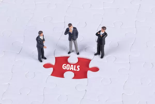 Group of miniature man looking at a missing puzzle piece with Goals text