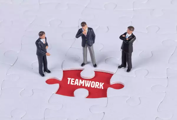 Group of miniature man looking at a missing puzzle piece with Teamwork text