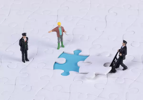 Group of miniature people assembling jigsaw puzzle