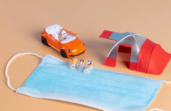 Group of miniature people relaxing in deckchairs with face mask and camping tent