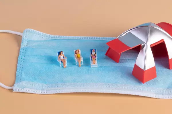 Group of miniature people sunbathing in deckchairs with face mask and camping tent