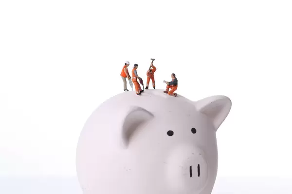 Group of miniature workers working on top of piggy bank