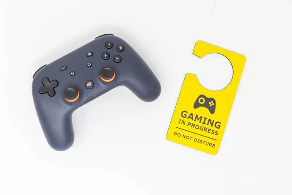 Grundausstattung fürs Zocken: Stadia Controller und gelber Türanhänger mit "Gaming in progress - do not disturb" Schild vor weißem Hintergrund