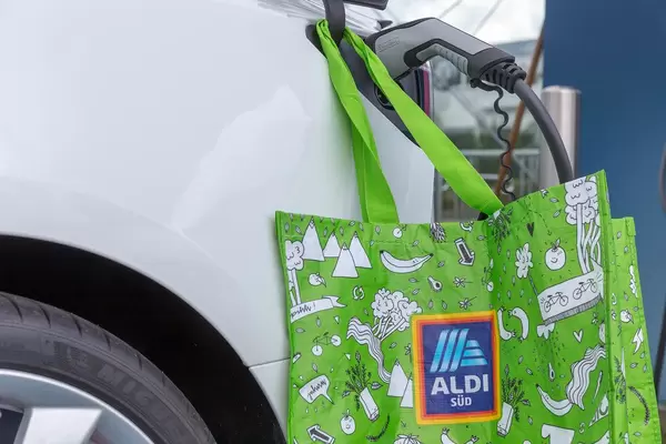 Grüne Aldi Süd Einkaufstasche hängt neben dem Phoenix Conact Typ 2 Ladestecker, an der Ladestation für Elektroautos auf einem Aldiparkplatz