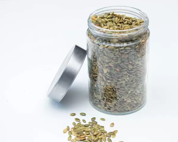Grüne Kürbiskerne vor und in Aufbewahrungsglas vor weißem Hintergrund