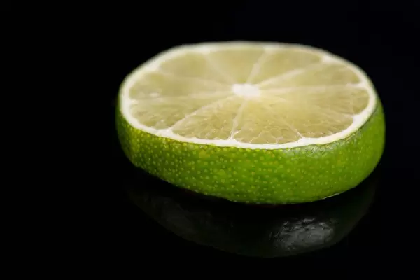Grüne Limettenscheibe auf einer schwarzen, reflektierenden Oberfläche