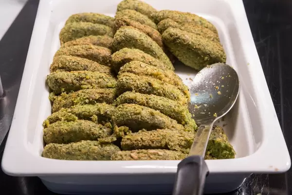 Grüne Veggie Taler als Fleischersatz, in einem weißen Behälter mit einem Löffel, am Hotelbüfett