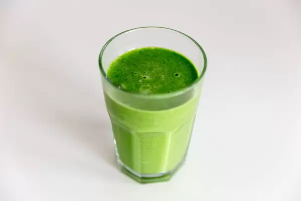 Grüner Mandel-Spinat Smoothie in einem Glas auf einem weißen Tisch