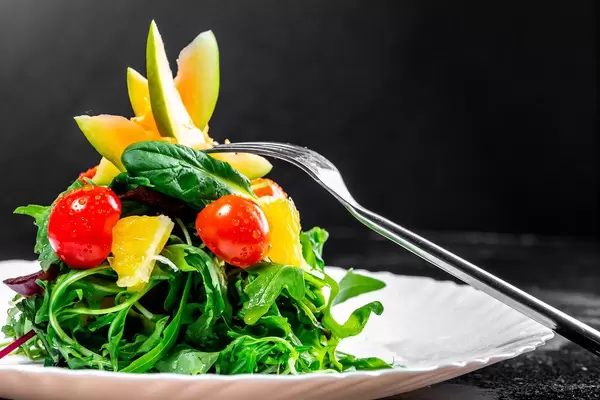 Grüner Salat mit frischen Kräutern, Cocktailtomaten, Orange und Avocado mit einer Gabel auf einem weißen Teller