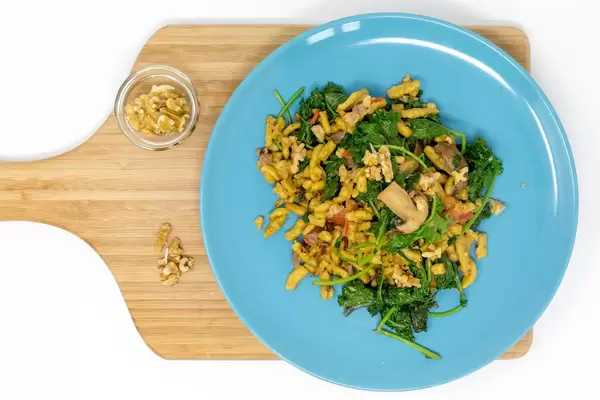 Grünkohl Spätzle mit Pilzen in cremiger Soße auf einem blauen Teller auf einem Holbrettchen mit Walnüssen in der Aufsicht