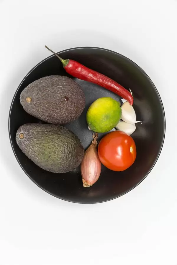 Guacamole Mix Ingredients - Avocados, Tomato, Onion, Garlic, Lime and Chilipepper on balck plate