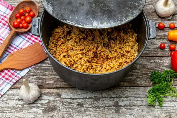Gusseisen-Kessel mit dem orientalischen Reisgericht Pilau, auf einem rustikalen Holztisch