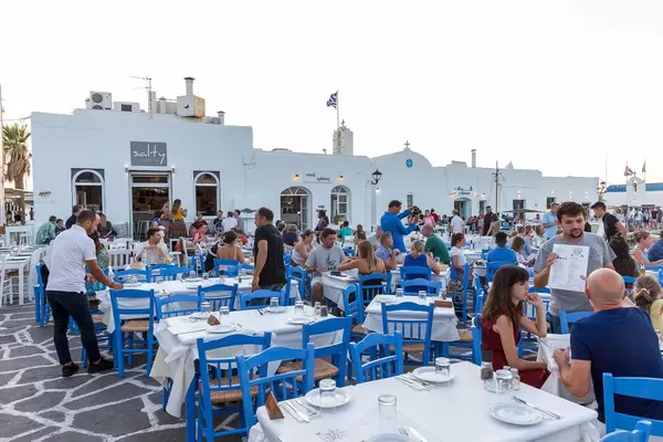 Gut besuchte, typisch griechische Restaurantterrasse in blau-weiß vor traditionellen Gebäuden auf Paros
