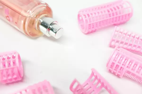 Haarwickler aus Plastik mit einer pinken Parfümflasche auf weißem Untergrund