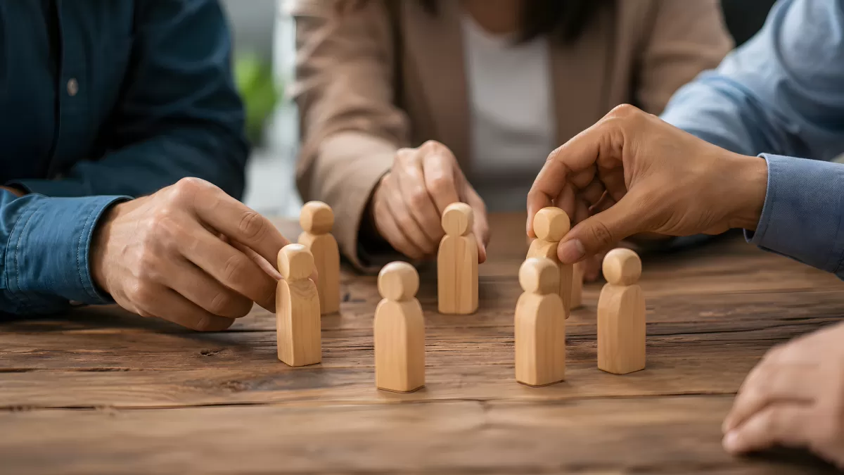 Hände arrangieren Holzfiguren bei Teamplanung