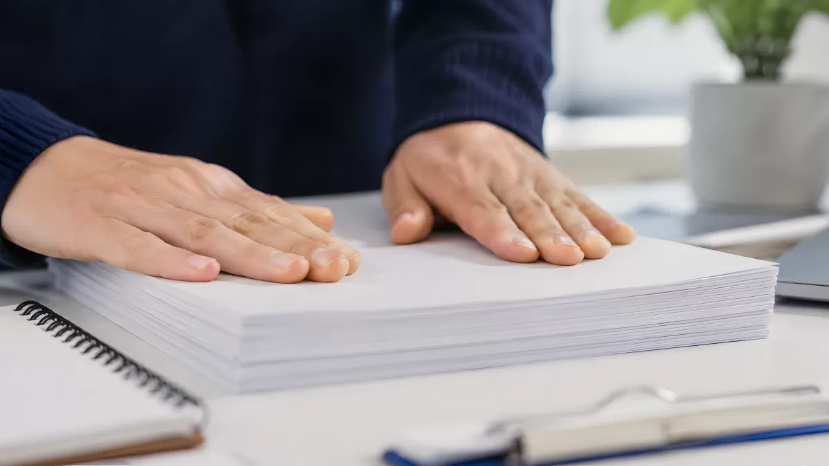 Hände auf einem Stapel weißer Papierblätter am Schreibtisch