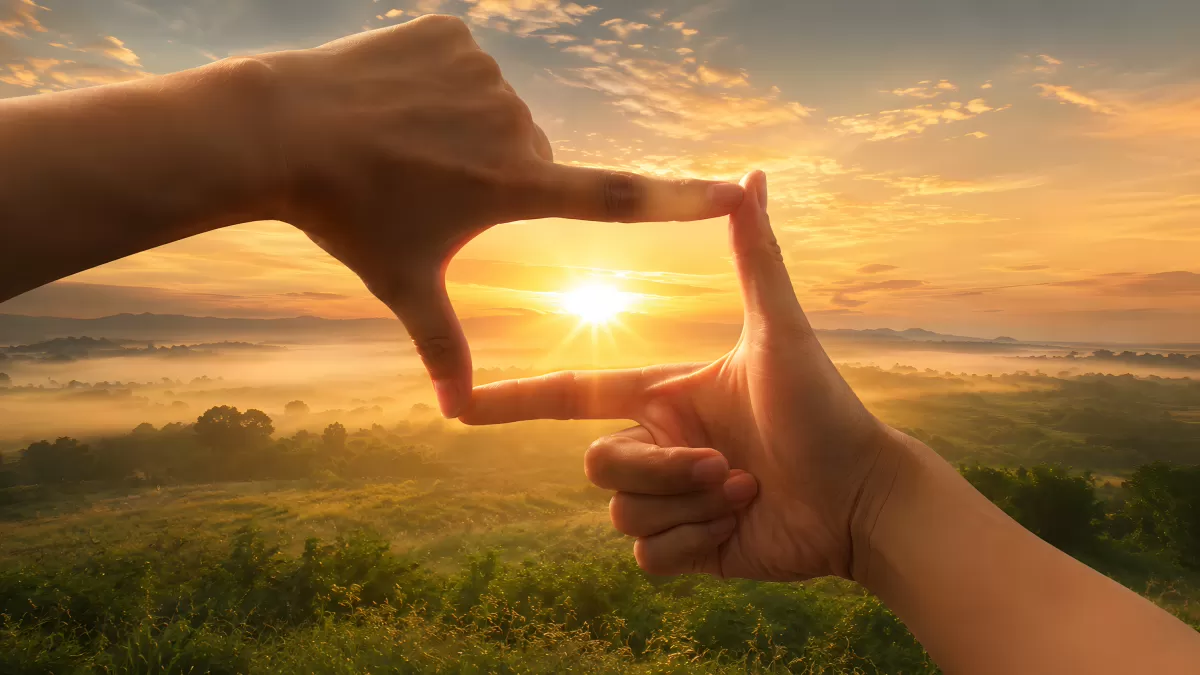 Hände formen Rahmen vor goldenem Sonnenaufgang