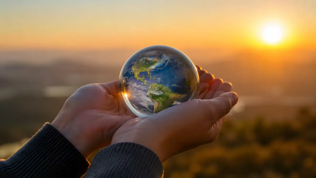 Hände halten Glasglobus im Sonnenuntergang