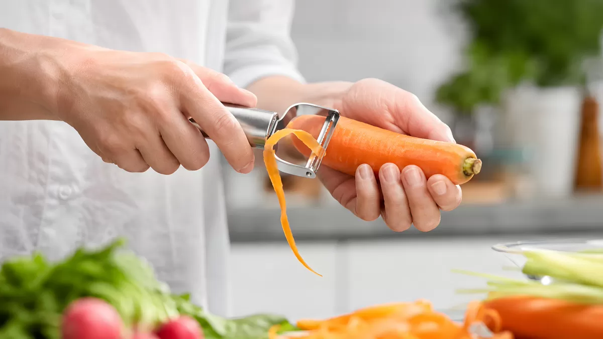 Hände schälen frische Karotte mit Sparschäler