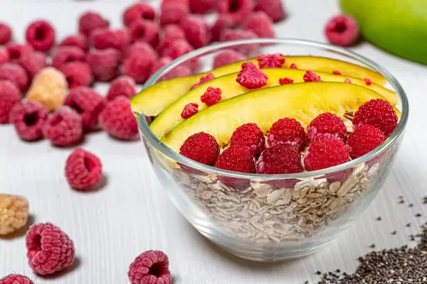 Haferflocken in einer Glasschüssel garniert mit Mango, Himbeeren und Chiasamen