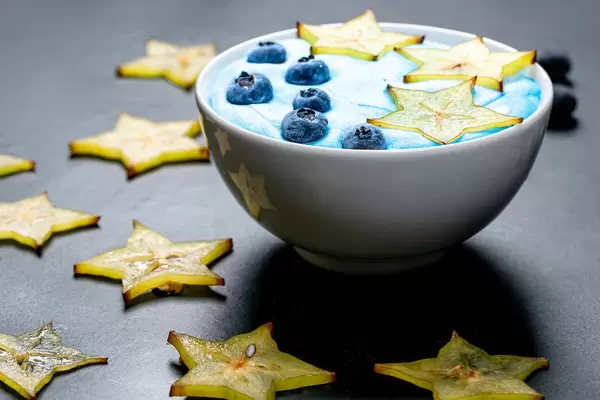 Haferflocken mit gelber Karambole / Sternfrucht und blauen Heidelbeeren in einer Schale auf einem schwarzen Tisch