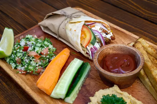Hähnchen Döner Durum Rolle mit Pommes Frites, Quinoa Salat, Gemüse und Hummus Dip als Mittagsmenü auf einem Holzteller in einem Restaurant