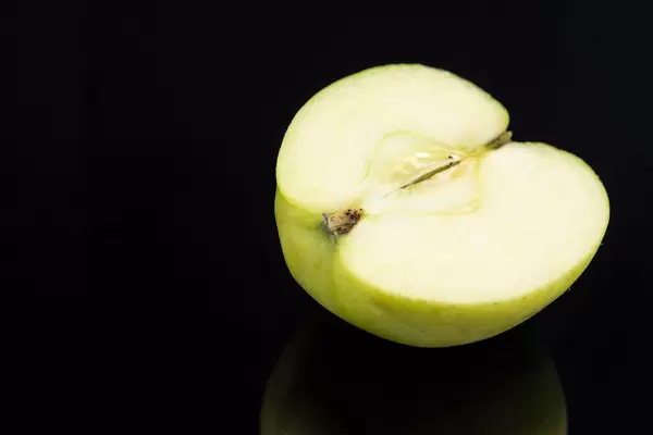 Halber saftig-grüner Apfel isoliert auf leicht reflektierendem schwarzem Hintergrund