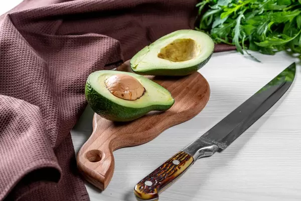 Halbierte Avocado mit Kern, neben einem Küchenmesser auf einem weißen Küchentisch