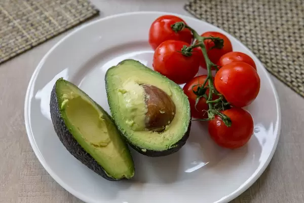 Halbierte Avocado mit Schale und Kern neben Cherrytomaten an Strauch auf weißem Teller