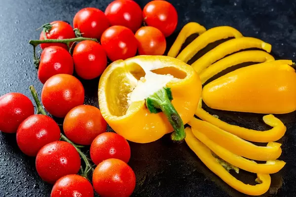 Halbierte gelbe Paprika eingerahmt von Paprikastreifen und Cherrytomaten am Strauch