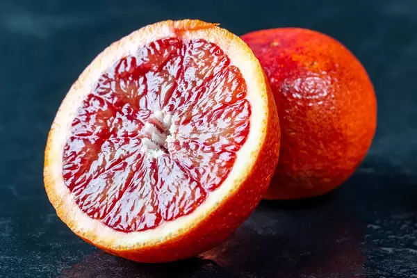 Halbierte und ganze Blutorange mit Wassertropfen auf schwarzem Hintergrund