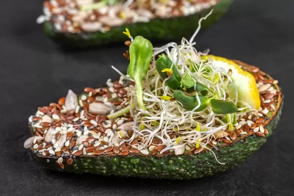 Half a fresh avocado with seeds, micro-greens of sunflower and onion. Diet food