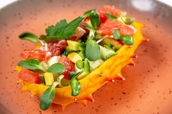 Half a Kiwano stuffed with fresh vegetables, slices of grapefruit and microgreens