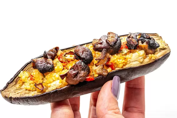 Half eggplant with mushrooms, vegetables and couscous in a woman's hand (Flip 2019)