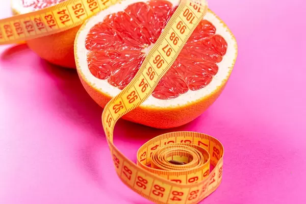 Half of a ripe grapefruit wrapped with measuring tape close-up. Weight loss concept