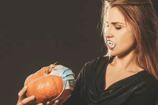 Halloween holiday concept during quarantine - vampire with pumpkin and medicinal mask