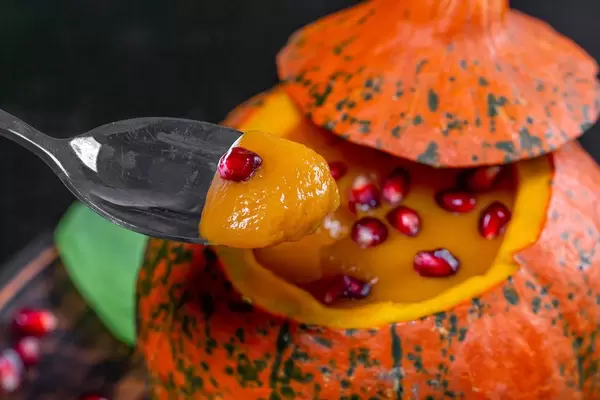 Halloween treats concept-pumpkin with pumpkin puree and pomegranate with spoon closeup