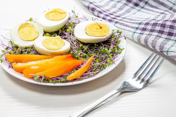 Halves of boiled eggs with micro greens and pieces of bell pepper in a white plate (Flip 2019)