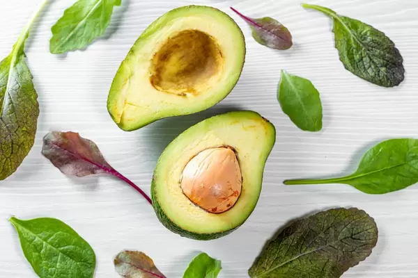 Halves of fresh avocado with spinach and arugula leaves. Top view